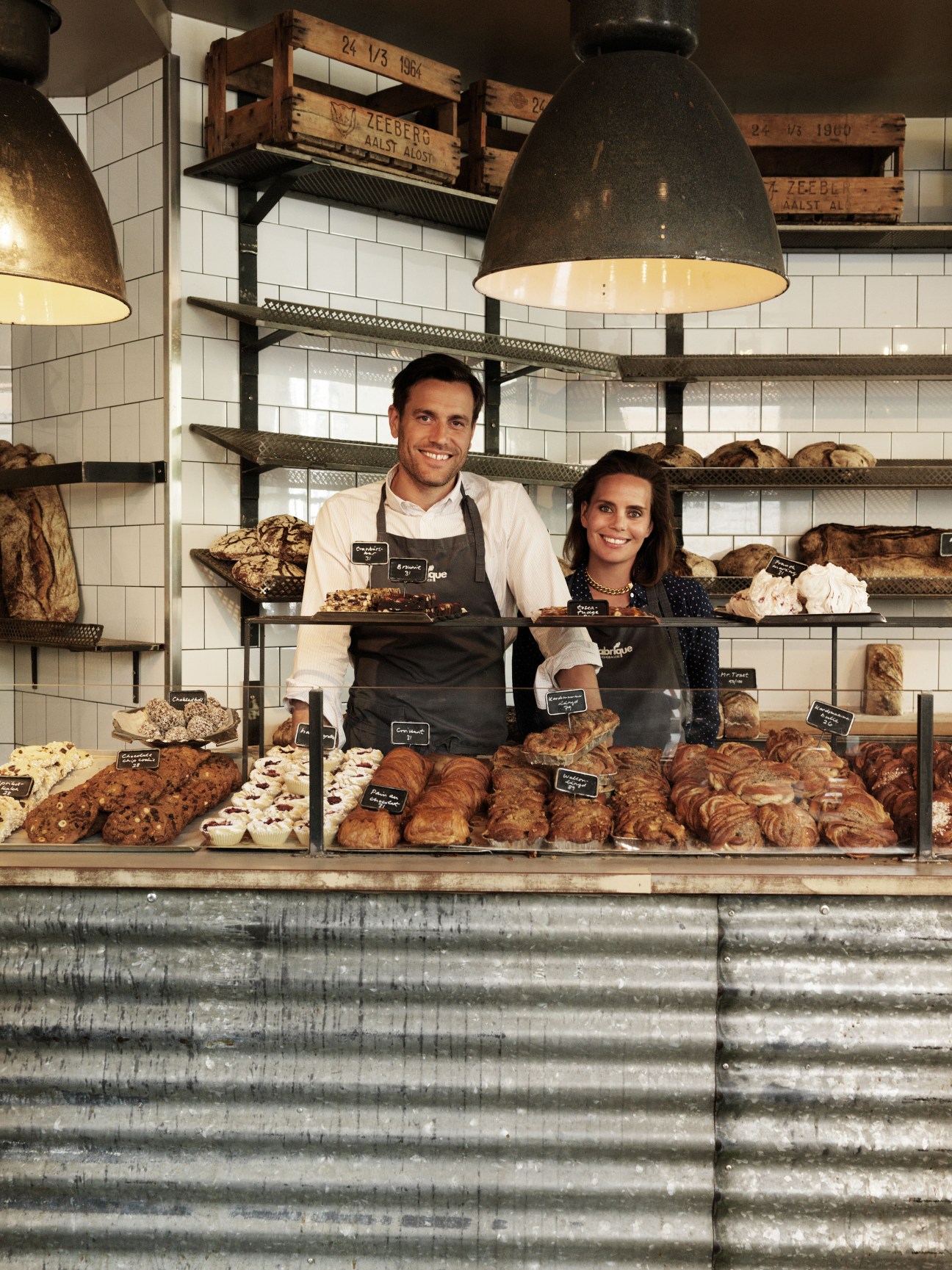 Two people standing behind a counter at Fabrique bakery with bread displayed on shelves behind them.