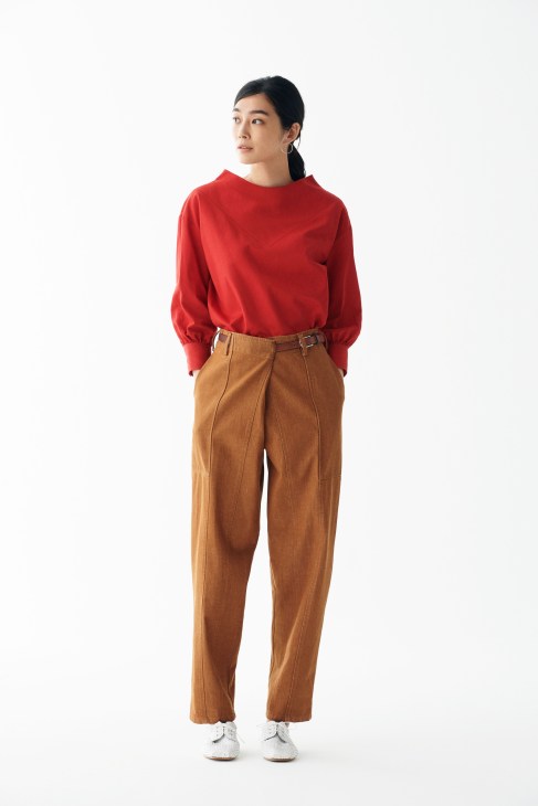 Woman wearing red pullover top by Atlantique Ascoli, tan trousers by Barena, white shoes by Emporio Armani, and earrings by Stephanie Cachard.