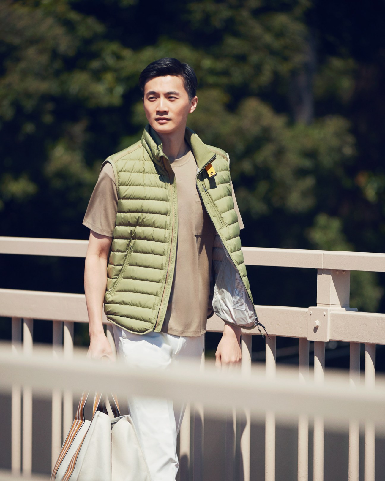 Man wearing a pale green quilted vest by Parajumpers over a t-shirt on a pedestrian bridge.