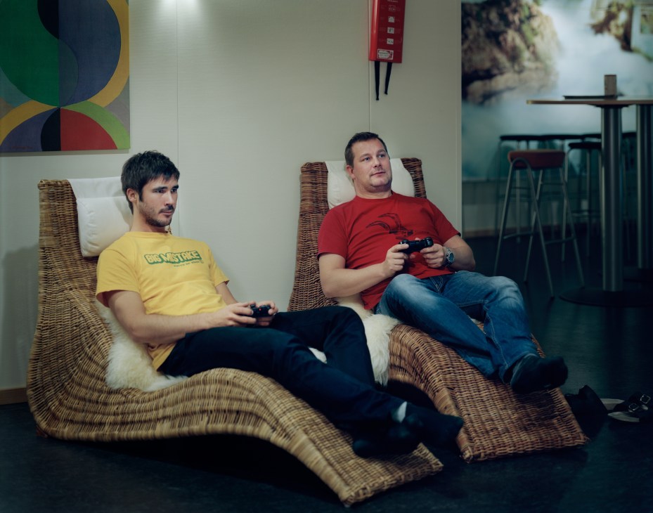 Two men sitting in wicker chairs holding game controllers in a modern office space.