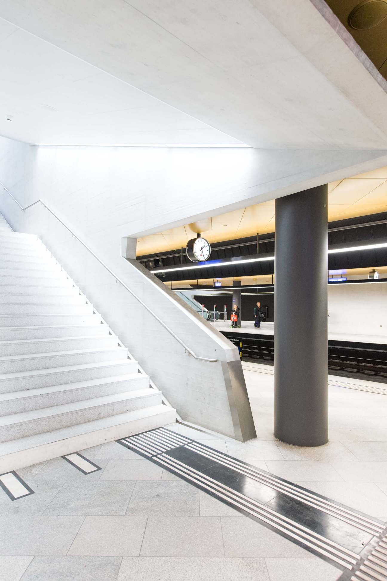 Interior of Zürich's Hauptbahnhof station showing concrete stairs, columns and minimalist design with platform below.