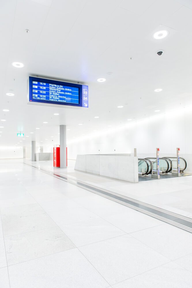 Modern minimalist metro station interior with blue departure board, white ceiling, and bike parking.