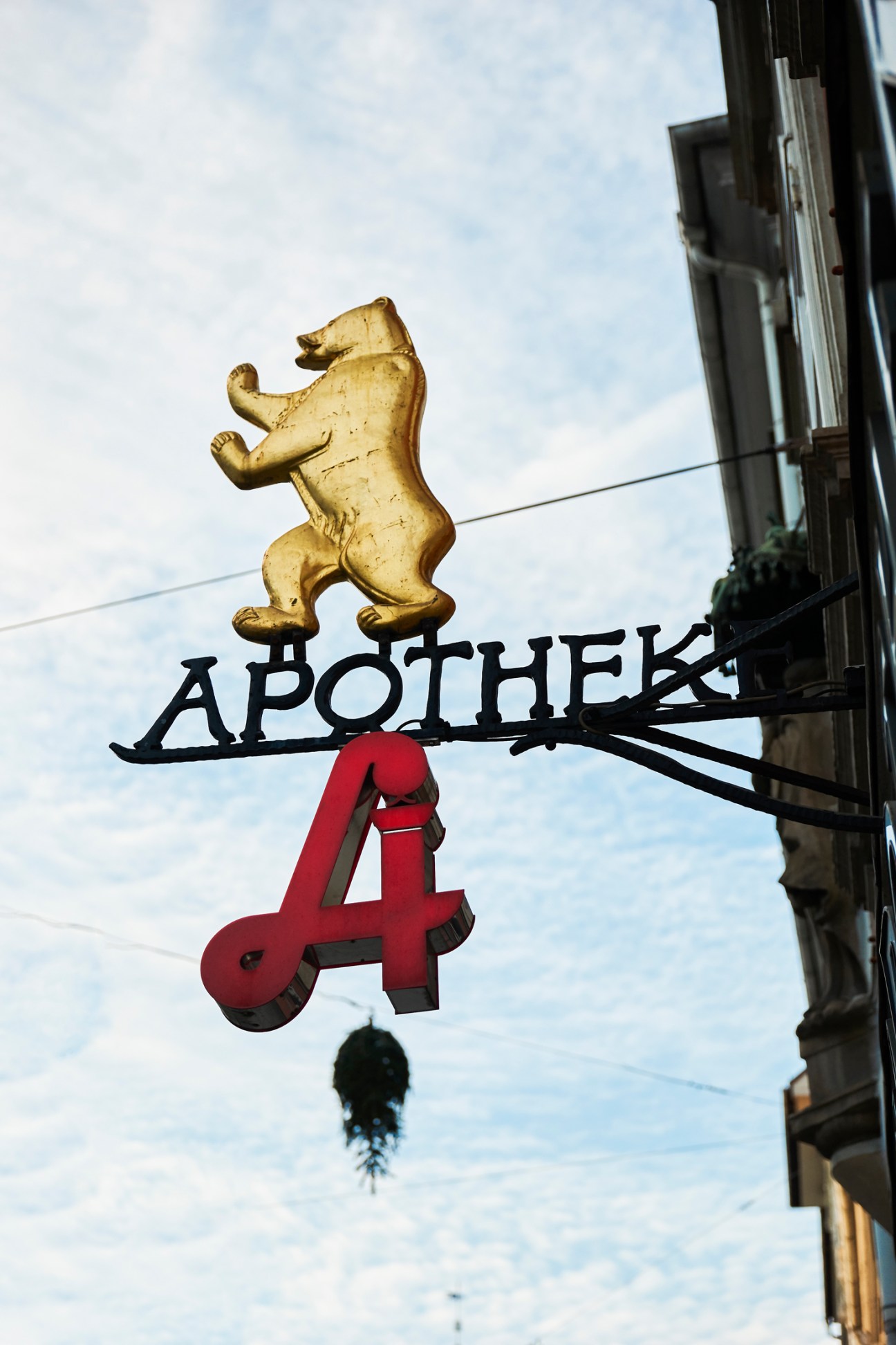 Ornate pharmacy sign with golden bear figure above black 'APOTHEK' lettering and red 'A' symbol