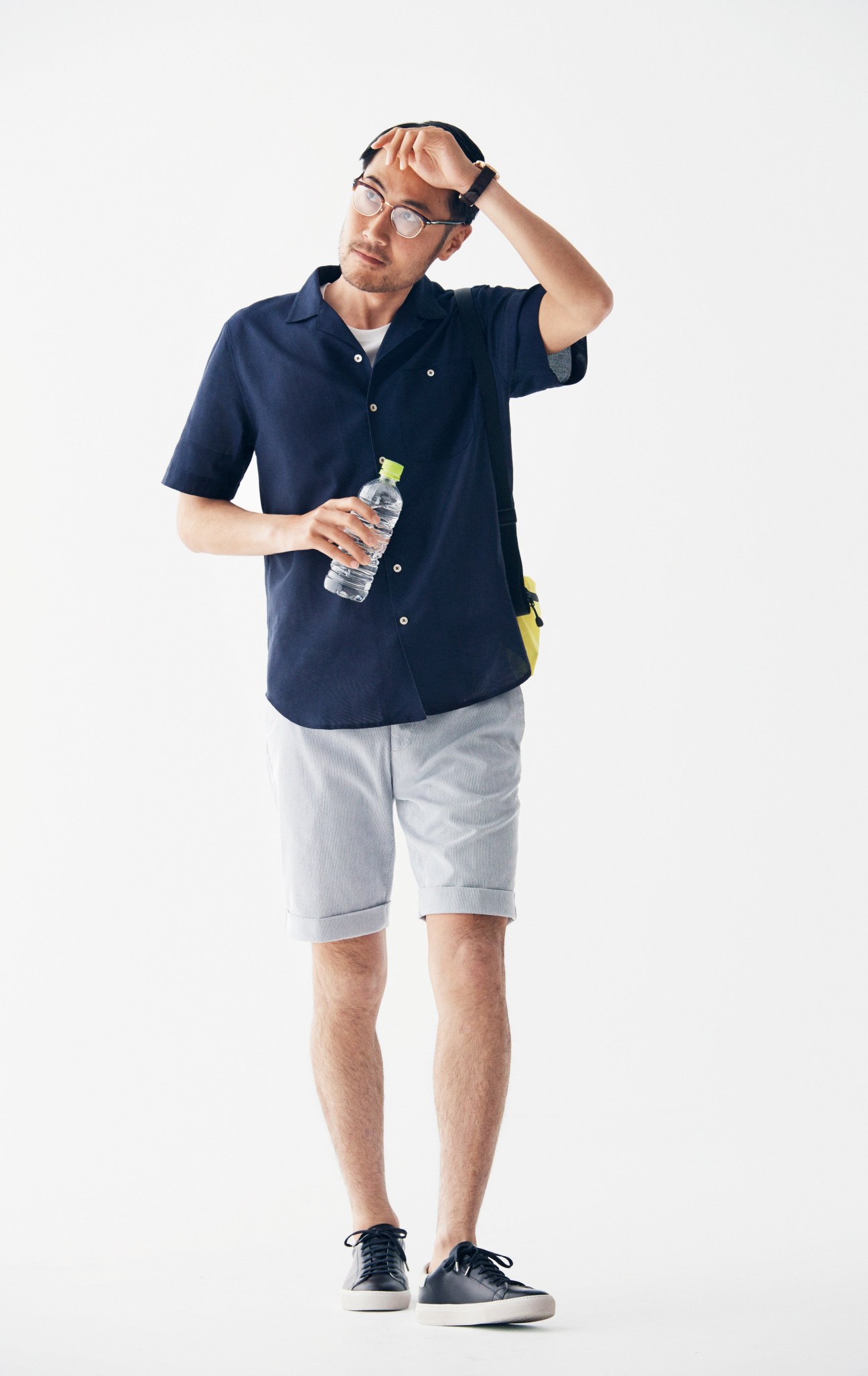 Man in navy shirt and light grey shorts holds water bottle while adjusting glasses.