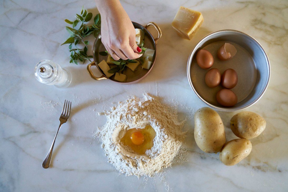 Cooking ingredients arranged on a marble surface including flour, eggs, potatoes, herbs, olive oil and a bowl of eggs at Rosewood Castiglion del Bosco.
