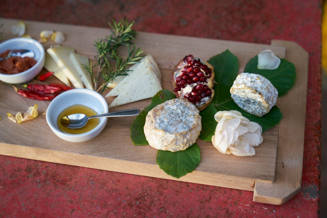 Tuscan charcuterie board with cheeses, pomegranate, olive oil, and herbs on wooden board.