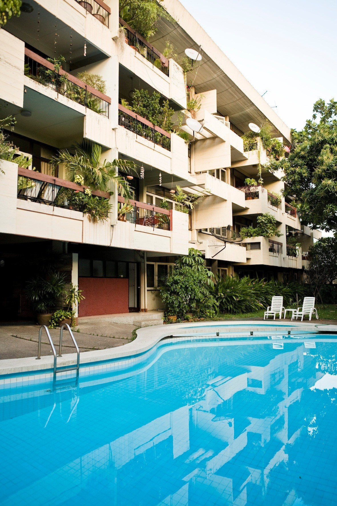 President House apartments in Bangkok with a swimming pool in the foreground and multi-story residential building with balconies and greenery.