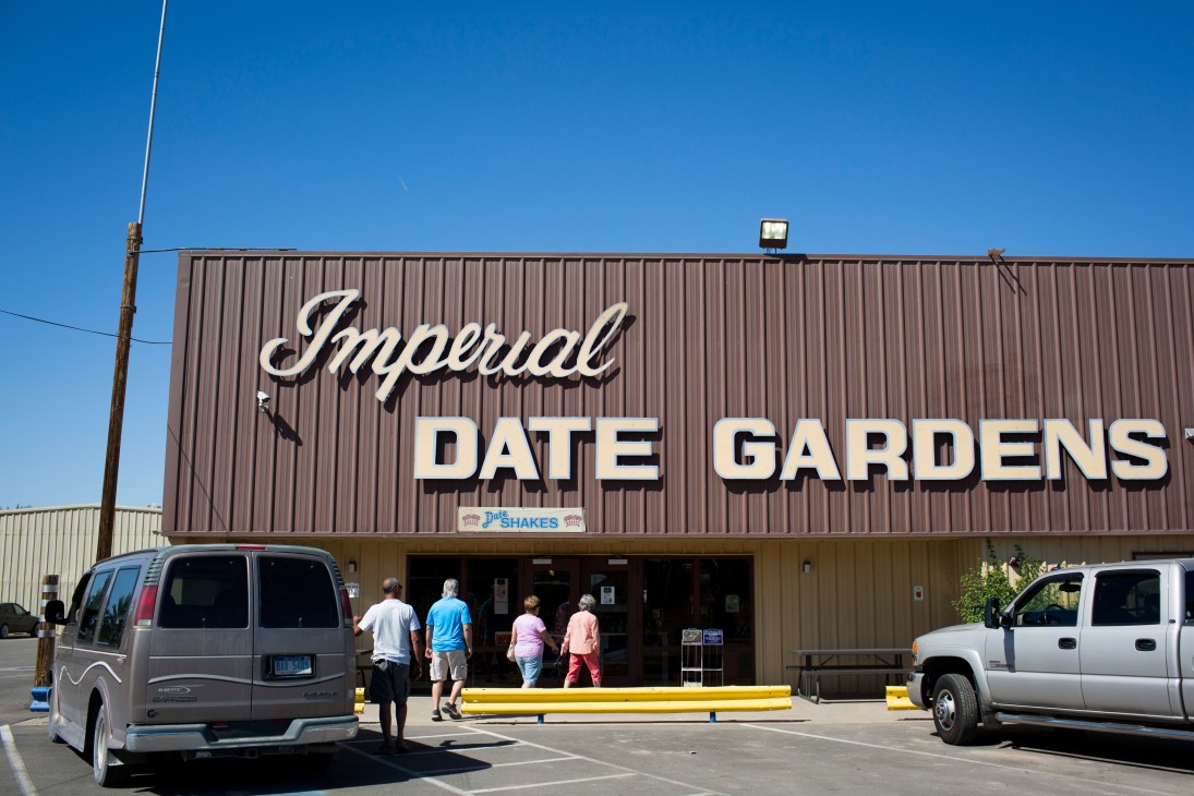 Imperial Date Gardens storefront with brown metal building and white signage under blue sky.