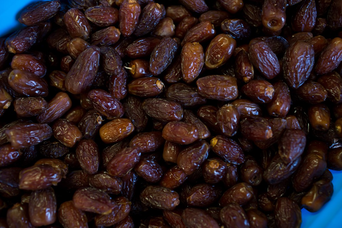 Close-up of plump medjool dates with glossy brown skin against a bright blue background.