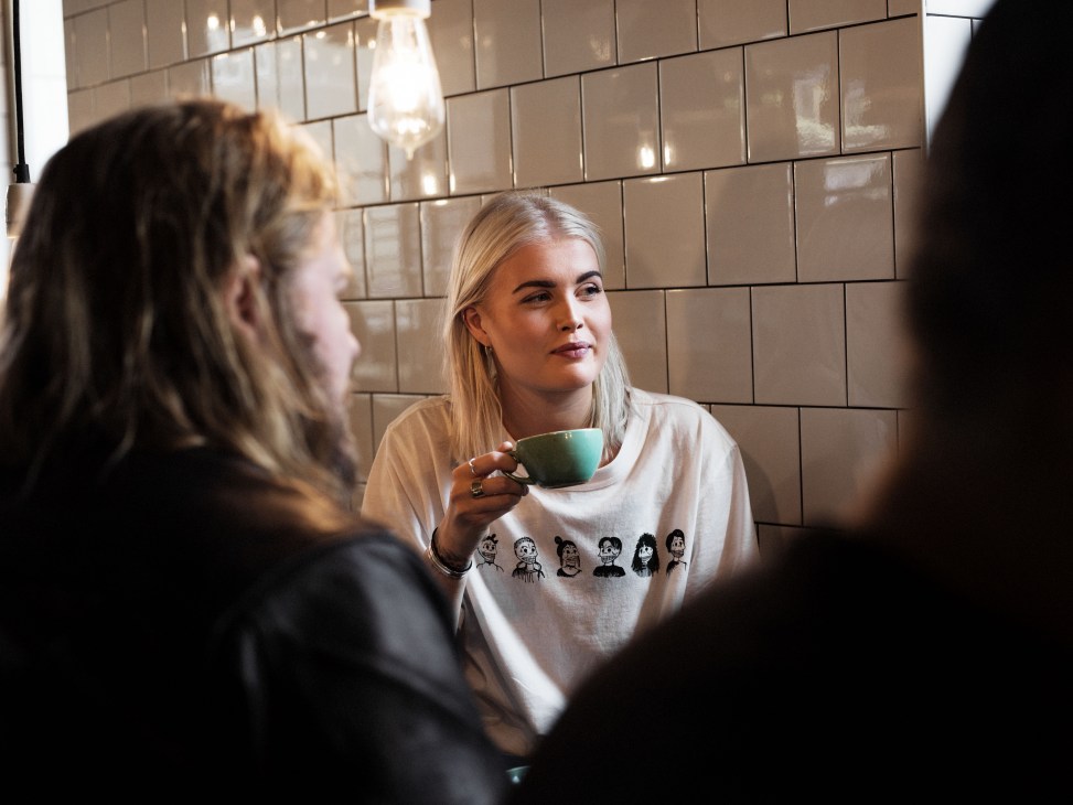 Two people chatting at a Fabrique bakery counter with tiled walls and pendant lighting.