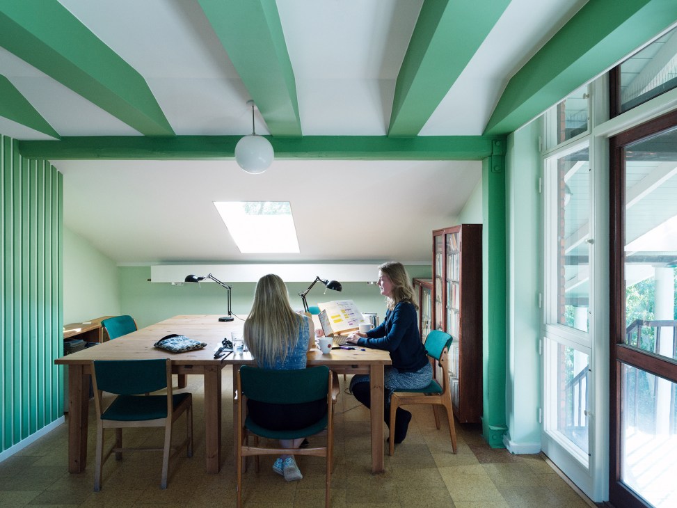 Two students study at a wooden table in a reading room with mint green striped walls and ceiling beams.