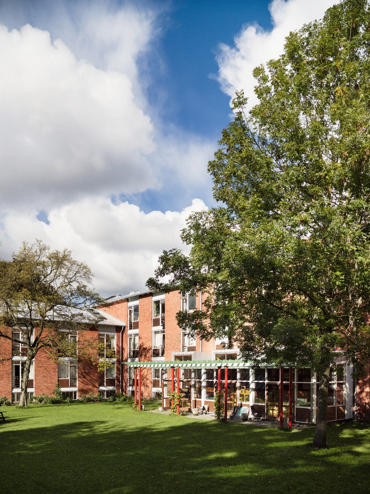 4th May College dormitory building in red brick with green and red pergola structure in courtyard overlooking gardens.