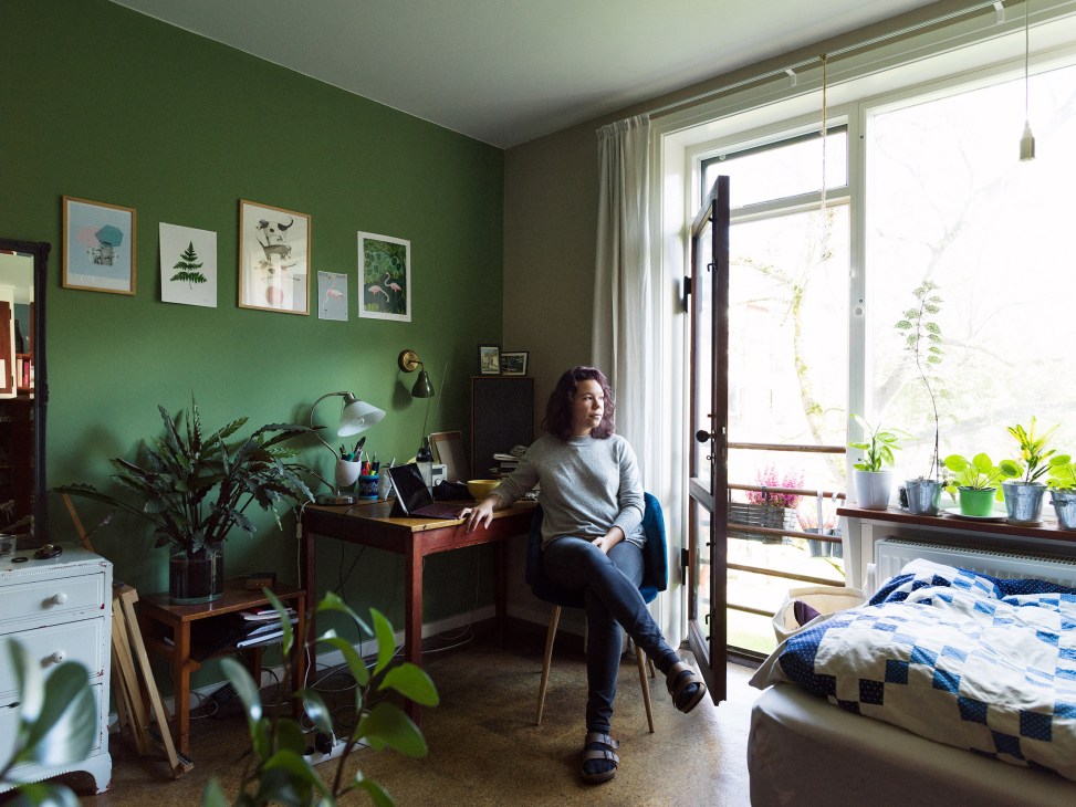 Student sits at desk in dormitory room with mint-green walls, wooden furniture and French balcony overlooking gardens.