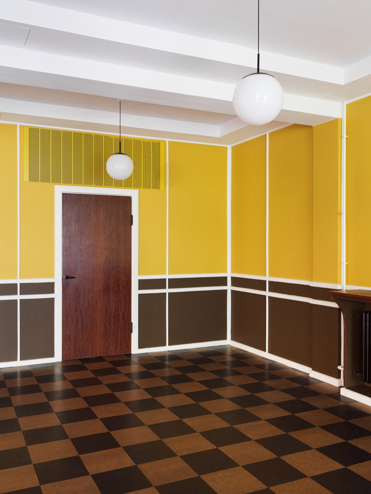 Bright yellow banquet hall with mahogany door, chequerboard cork floor, and pendant lighting.
