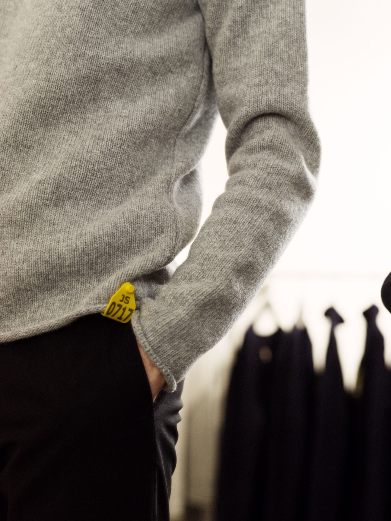 Close-up of a grey merino crewneck sweater with a yellow sheep tag label at the hem.
