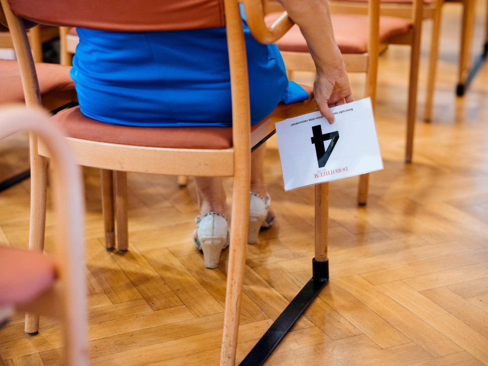 Person holding auction paddle number 4 while seated on wooden chair at Dorotheum auction house
