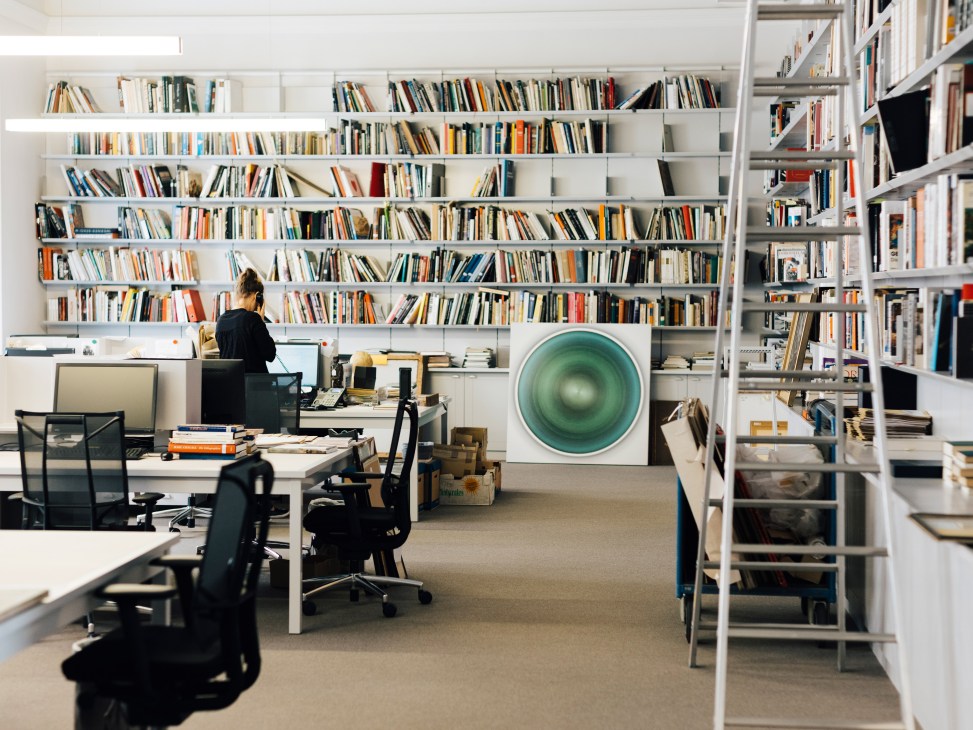 Person working at desk surrounded by floor-to-ceiling bookshelves in white modern office space