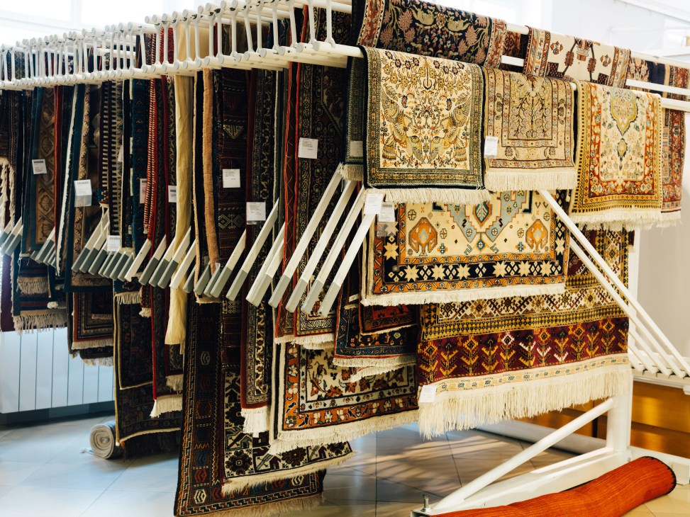 Display of oriental rugs hung on white racks in a showroom with geometric patterns and fringed edges