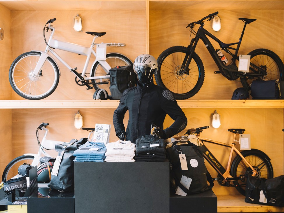 Wingwheels shop interior with electric bikes displayed on wooden shelves and a mannequin wearing cycling gear.