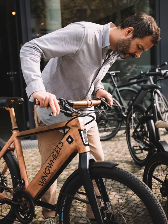 Man in casual shirt examining a Wingwheels electric bike with integrated battery in frame.