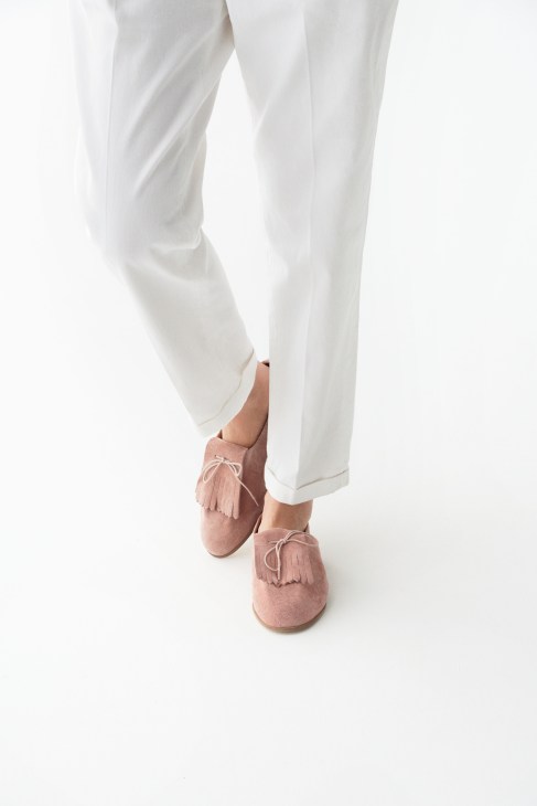 Person wearing white trousers and pink suede shoes with fringe detailing by Solovière.