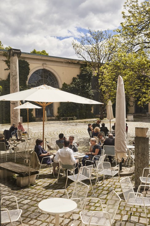 People dining outdoors at tables under umbrellas in the Glyptothek's classical courtyard.