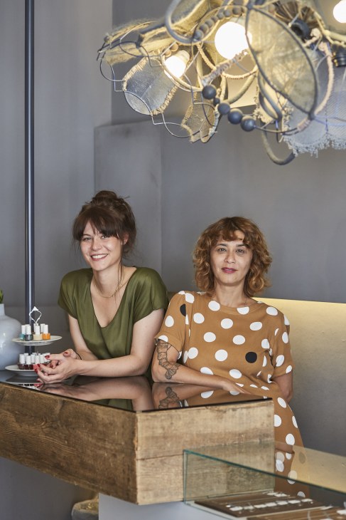 Two women at a retail counter under a decorative brass pendant light fixture.