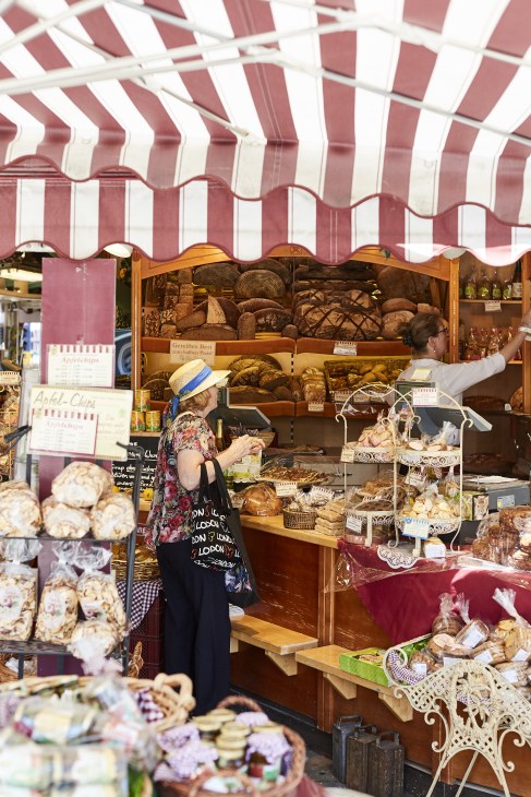 Vendor at Viktualienmarkt open-air food market stall with red and white striped awning displaying breads and baked goods.