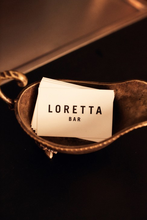 White business cards with Loretta Bar branding in black text placed in a copper-colored metal tray