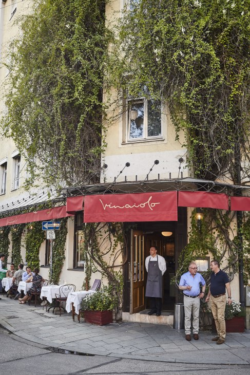 Vinaiolo Italian restaurant storefront with ivy-covered facade and red awning in Munich.