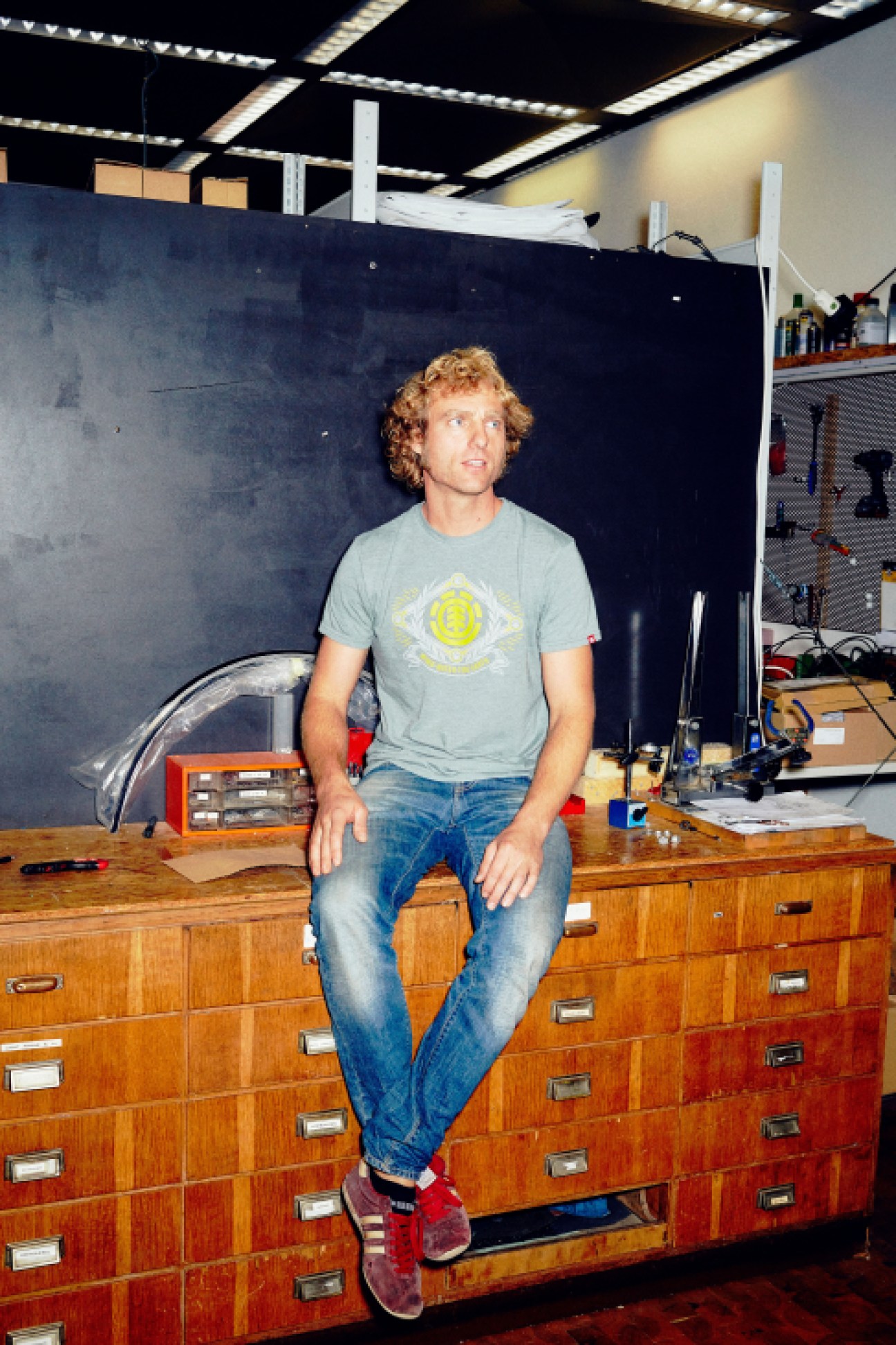David Horsch sits on a wooden workbench in Coboc's workshop with tools and equipment visible in the background.