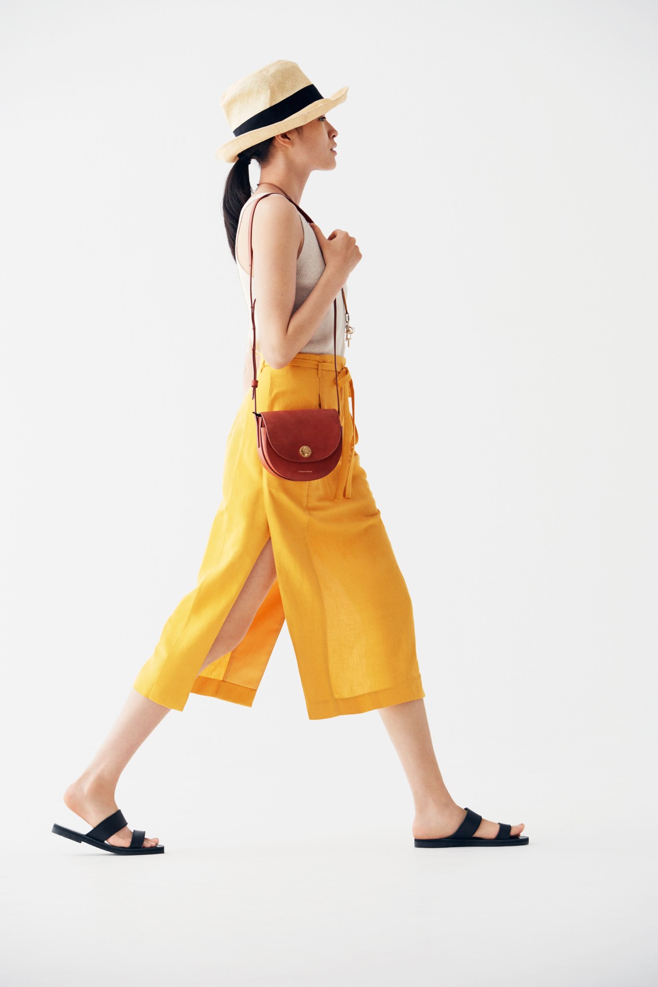 Woman in yellow skirt and straw hat walking with Mansur Gavriel shoulder bag.