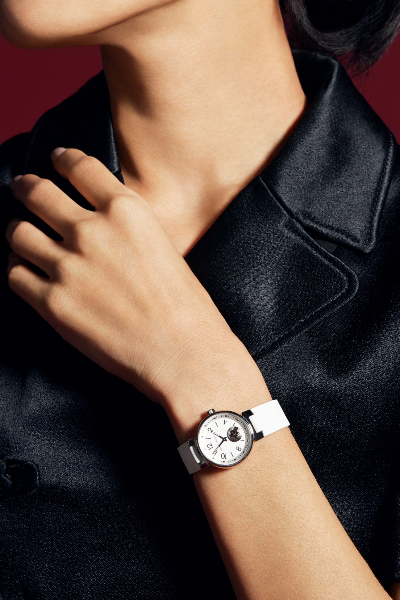 Woman in black dress with white collar detail and Louis Vuitton watch against red background