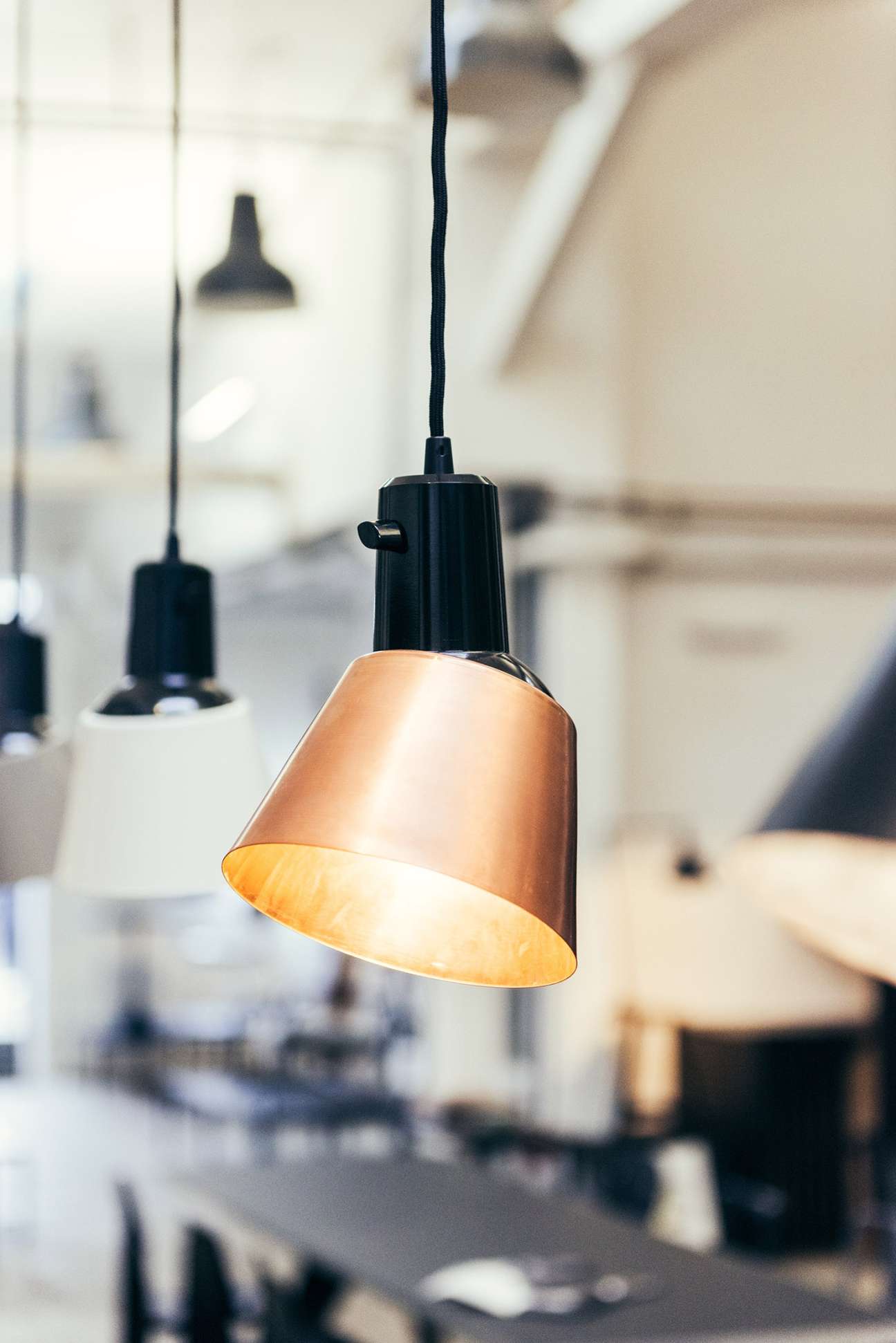 Midgard K831 pendant lamp with copper shade and black cord hanging in showroom.