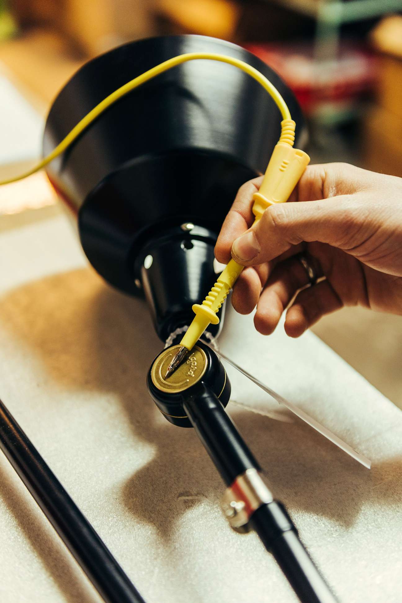 Hand holding a yellow cord connected to a black Midgard lamp during assembly in the workshop.