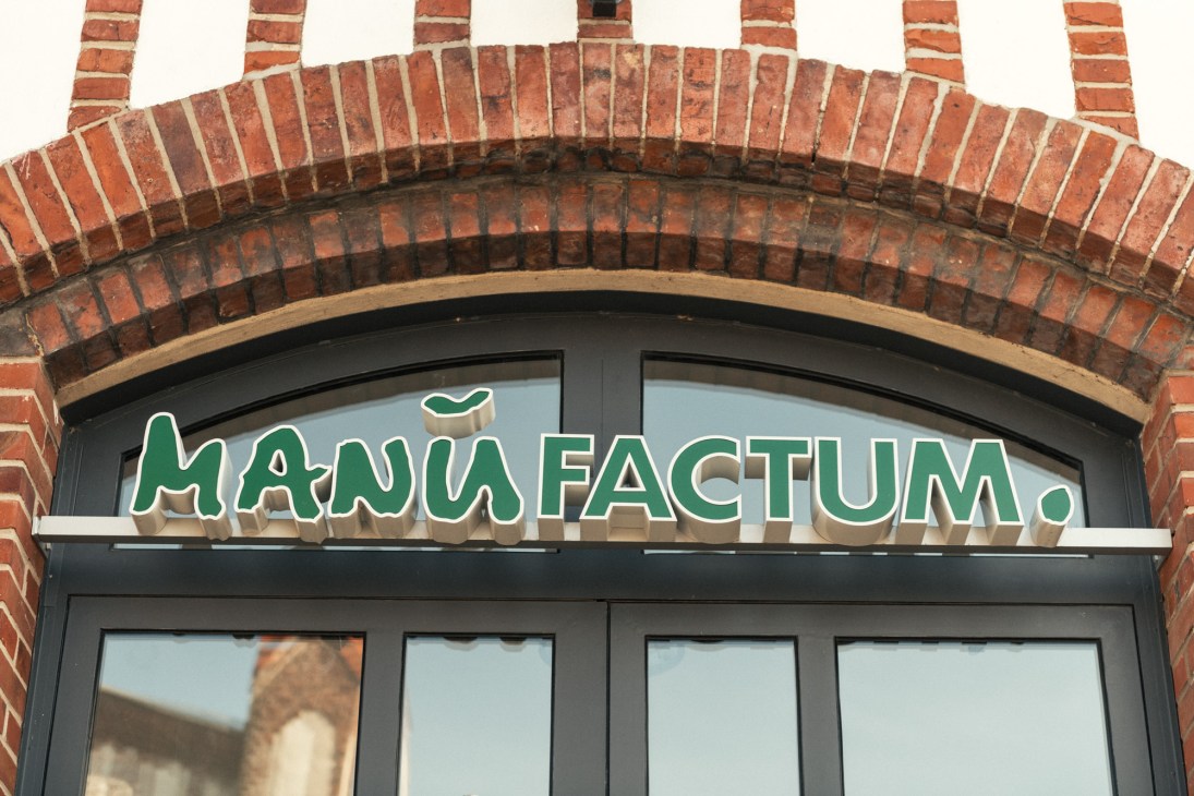Manufactum storefront with green lettered signage on a brick archway facade.