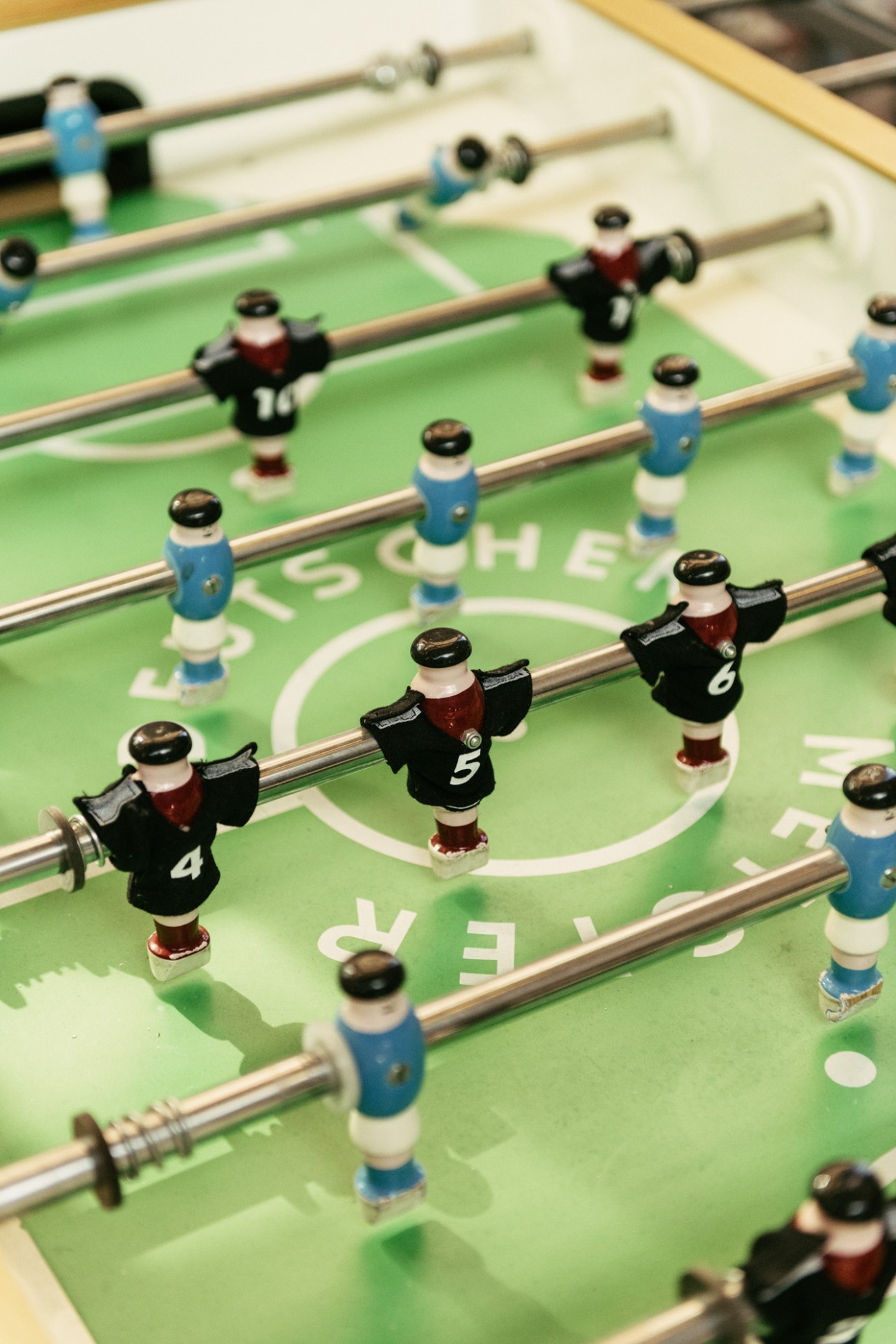 Close-up of a foosball table with black and blue player figurines on wooden rods against a green playing surface.
