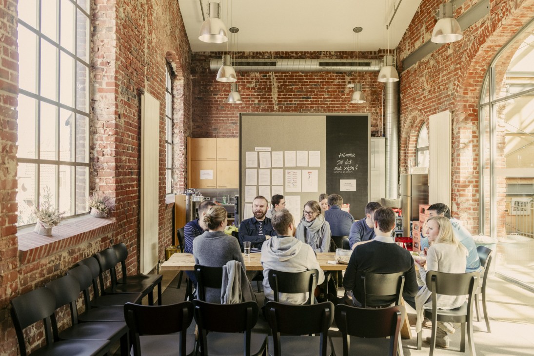 Employees gathered around a wooden table in the brick-walled canteen having a discussion.