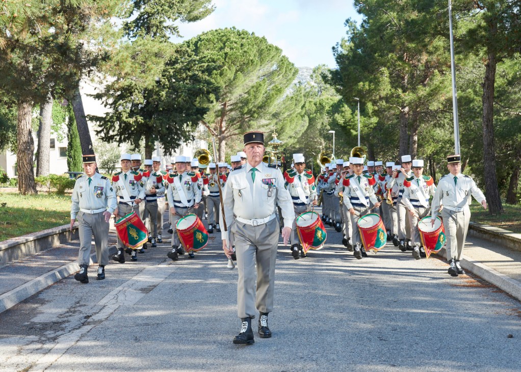 French Foreign Legion officer leading uniformed soldiers in ceremonial parade down tree-lined path
