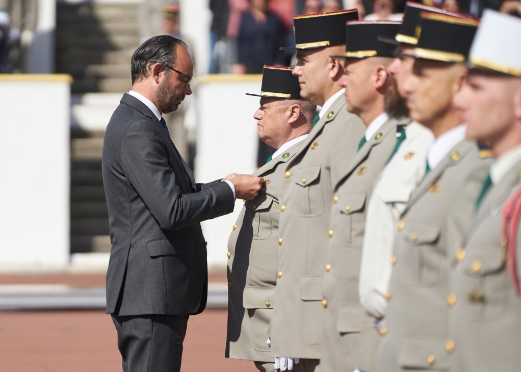 French Prime Minister Édouard Philippe awarding service medals to Foreign Legion soldiers in dress uniforms.