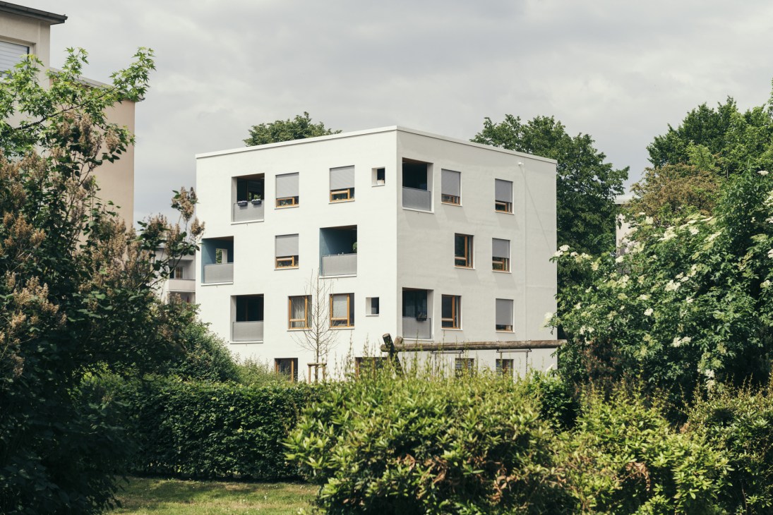 White four-storey Bremen Cube residential building surrounded by green vegetation and hedges.