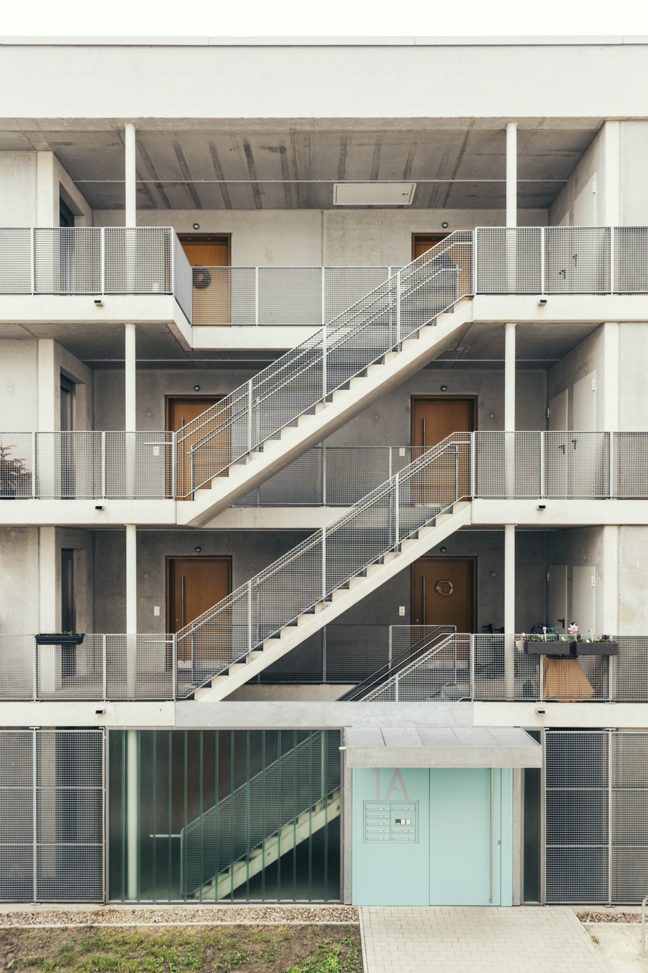 Multi-story residential building with open staircase, white railings, and wooden doors across multiple levels.