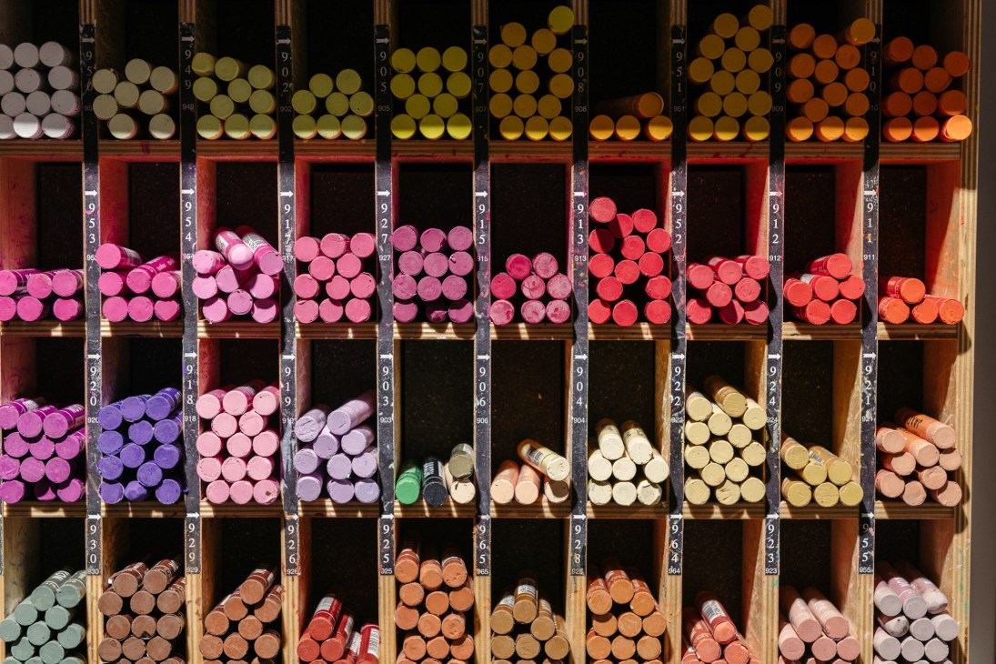 Shelving unit displaying colored pencils organized by shade from pink to yellow to orange at Modulor stationery shop.