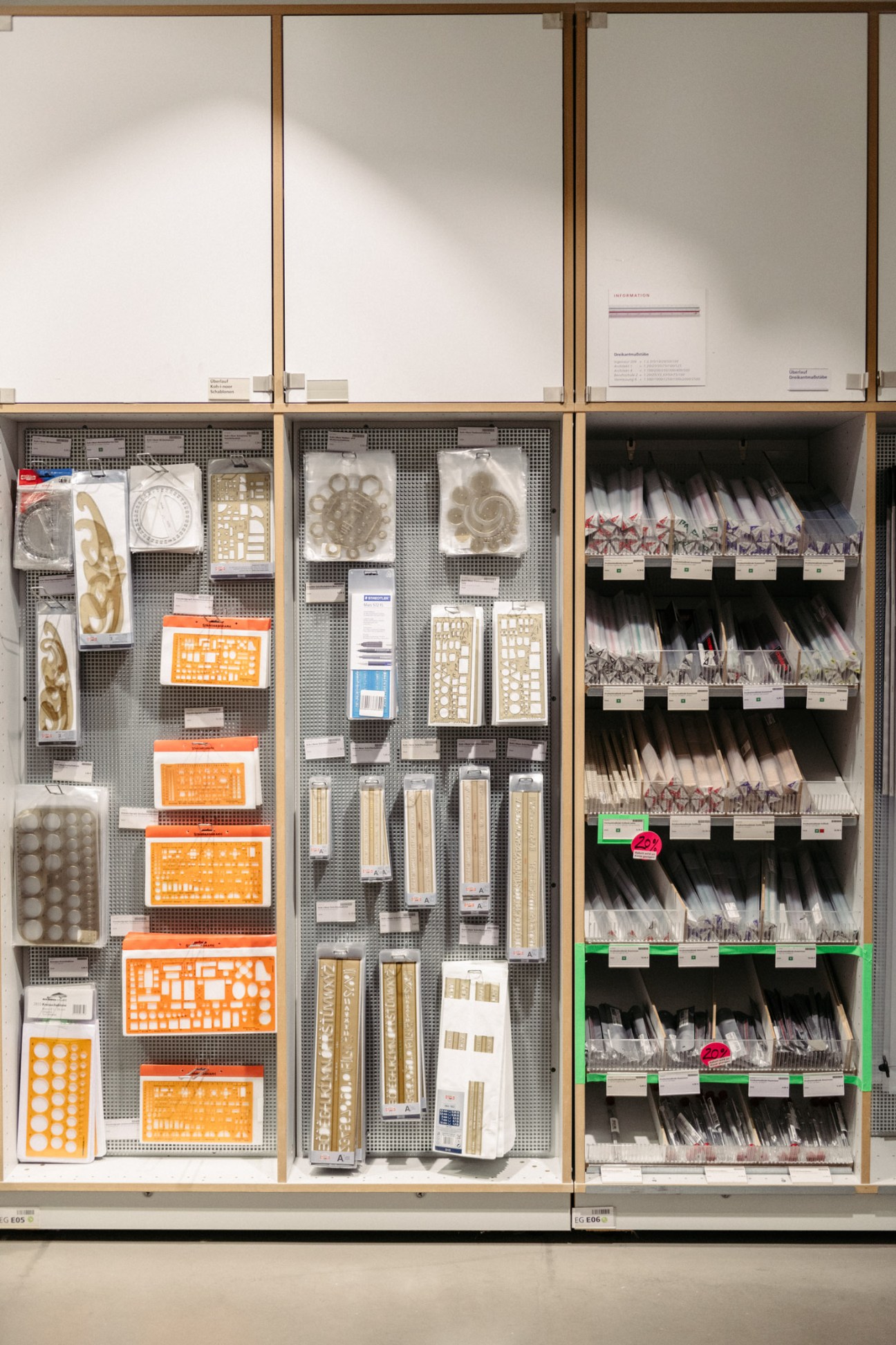 Modulor shop shelving displays architectural templates, stencils, and art supplies organized in wooden-framed compartments with metal mesh backing.