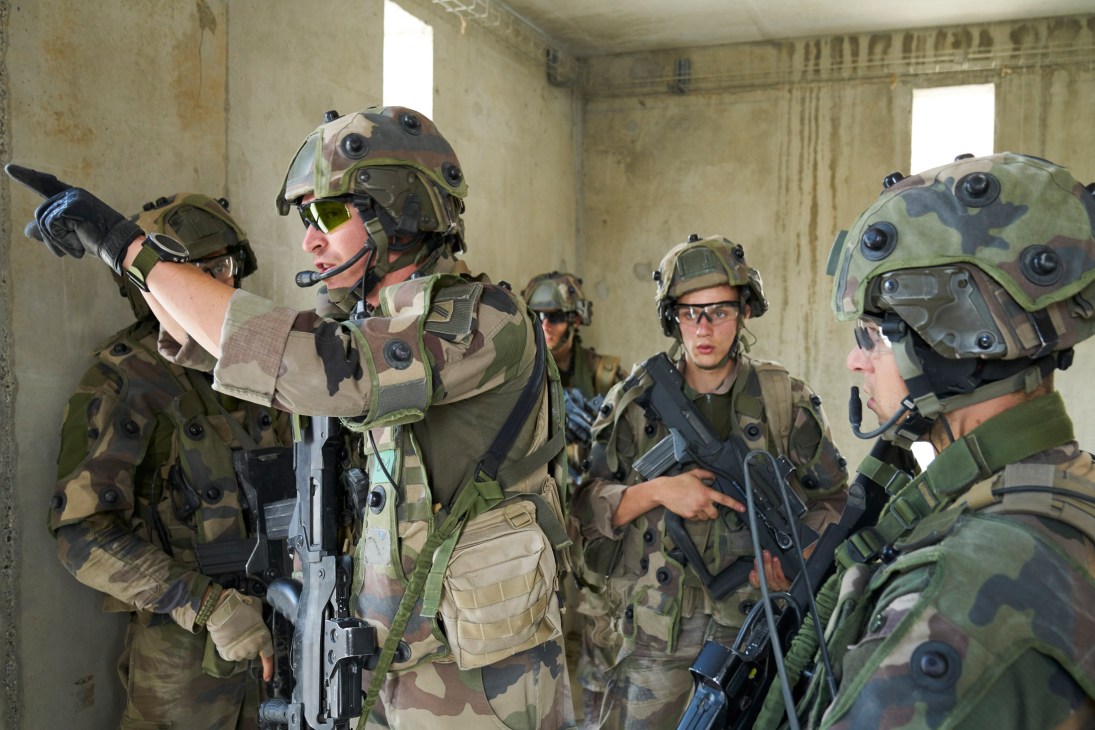 French Foreign Legion soldiers in combat gear and helmets inside a concrete building during training exercise.