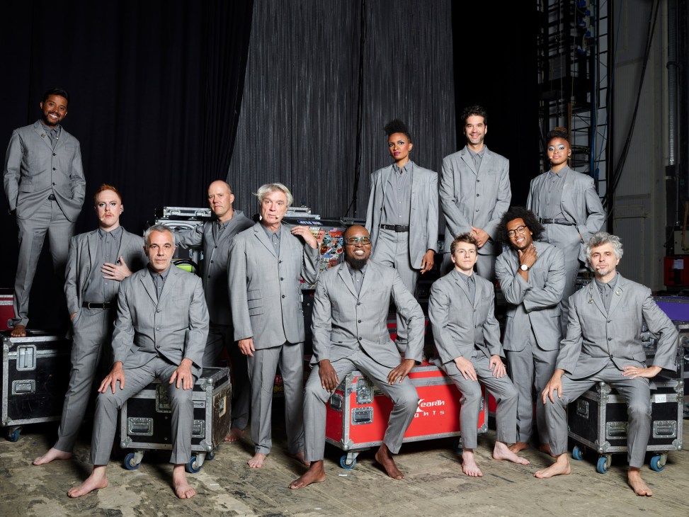 David Byrne and his diverse 11-member band in matching grey suits posing backstage barefoot.