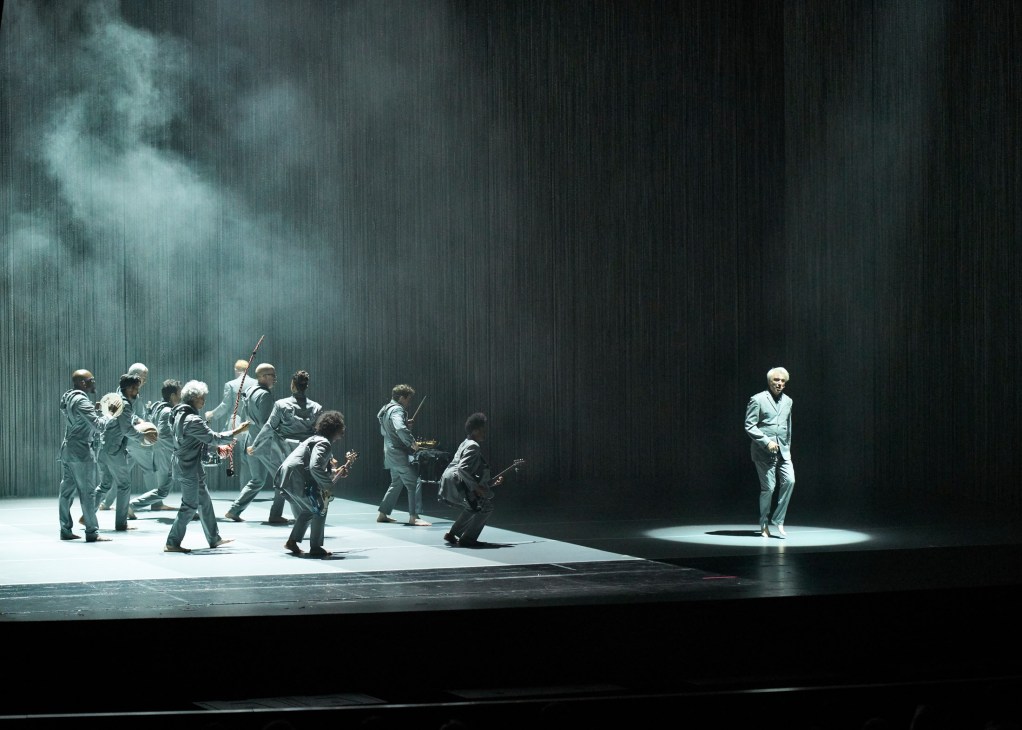 David Byrne and his band performing on stage with chainmail curtain backdrop during the American Utopia tour