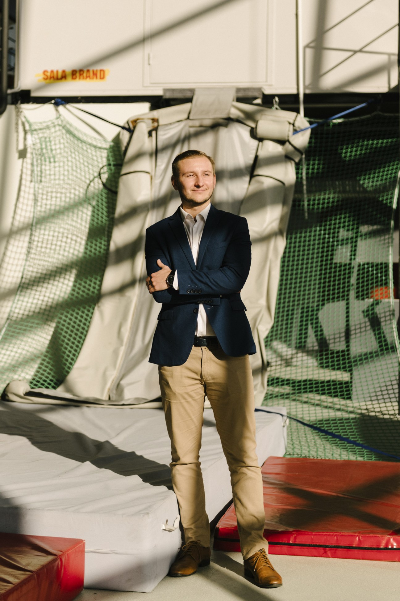 Man in navy blazer and tan trousers standing in front of Sala Brand signage and green netting