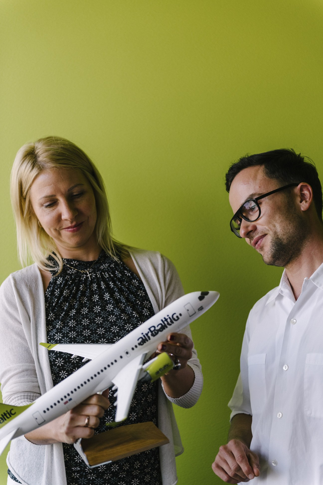 Two AirBaltic employees examine a model aircraft against a lime-green background
