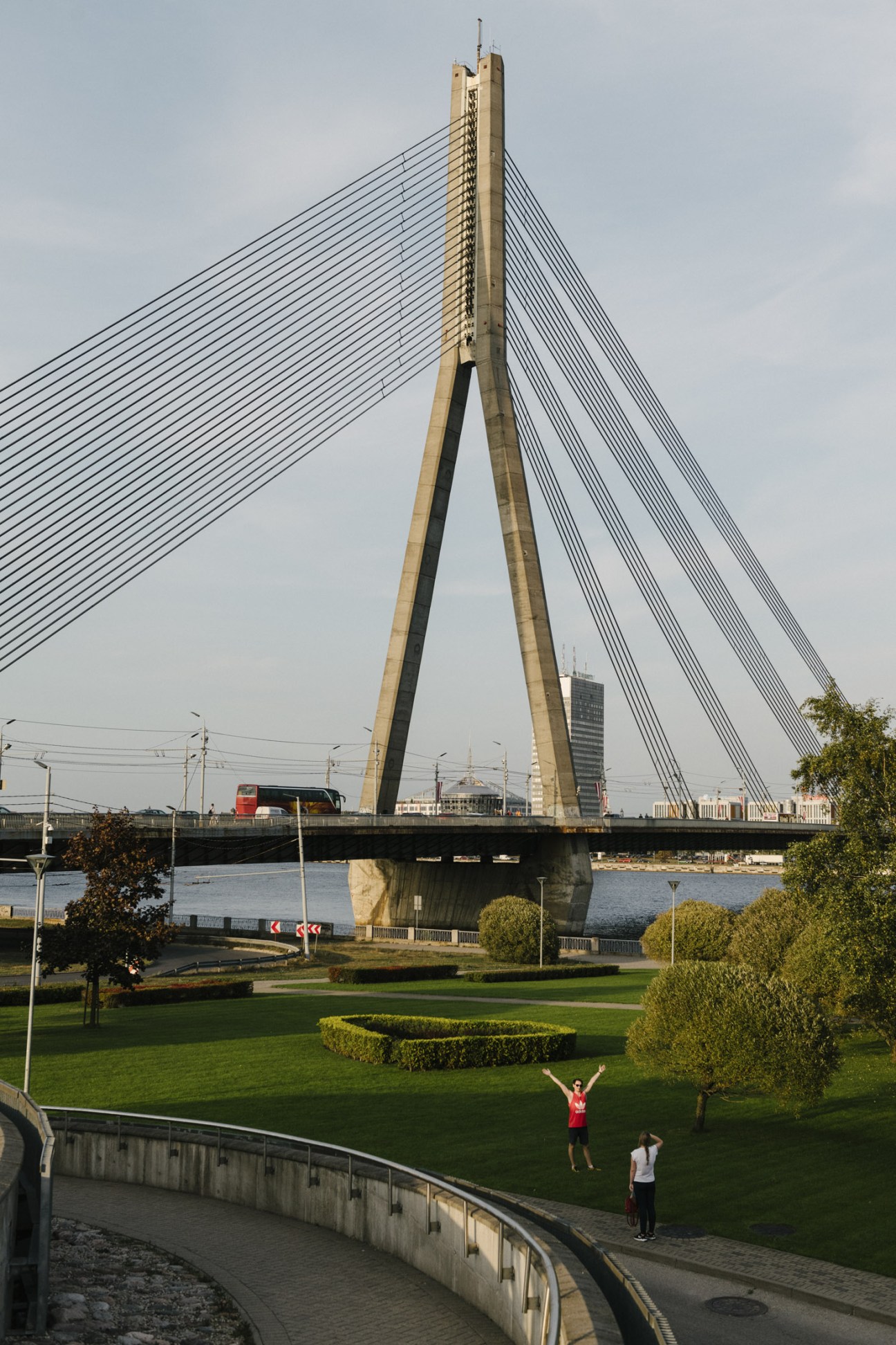 Vanšu Bridge spanning across river in Riga with people on grass below